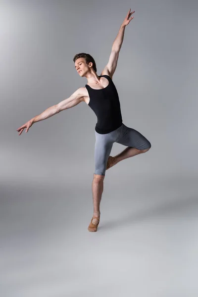 Elegante joven bailarina haciendo gestos mientras realiza danza de ballet en gris oscuro - foto de stock