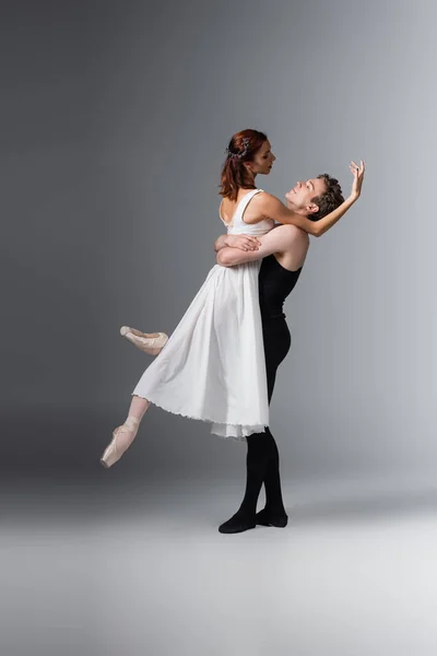 Comprimento total de bailarina levantar bailarina graciosa em vestido branco no cinza escuro — Fotografia de Stock