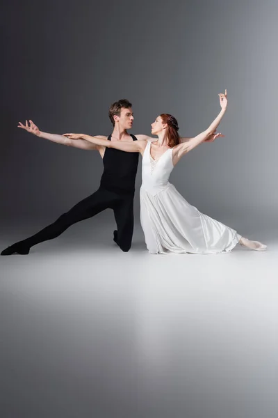 Comprimento total da bailarina no vestido branco dançando com o parceiro no cinza escuro — Fotografia de Stock