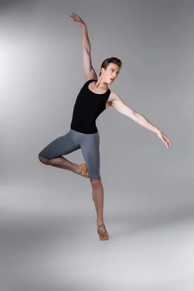Joven y elegante hombre haciendo gestos mientras realiza danza de ballet en gris oscuro - foto de stock