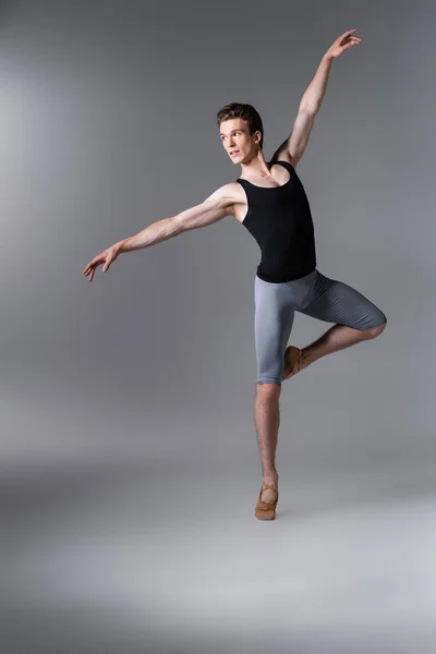 Joven bailarina en camiseta sin mangas mientras realiza danza de ballet en gris oscuro - foto de stock