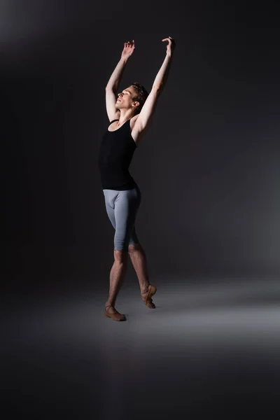 Молодой и грациозный мужчина с протянутыми руками исполняет балетный танец на черном — стоковое фото
