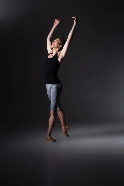 Young and graceful man with outstretched hands performing ballet dance on black — Stock Photo