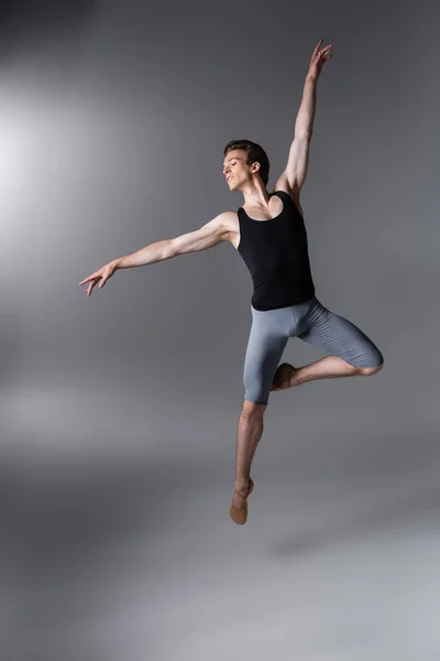 Joven y elegante bailarina de ballet haciendo gestos mientras levita sobre gris oscuro - foto de stock