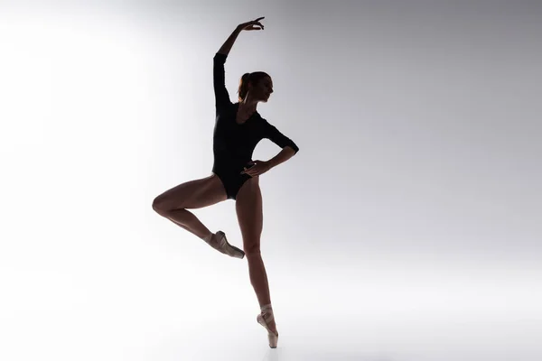 Silhouette of ballerina in bodysuit dancing on gray — Stock Photo