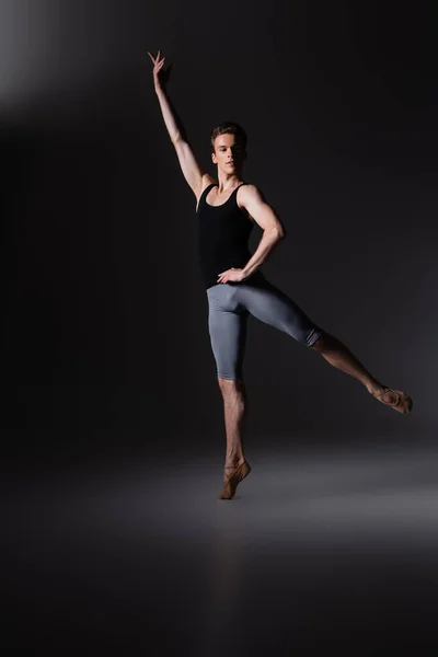 Витончений чоловік з простягнутою рукою виконує балетний танець на чорному — стокове фото