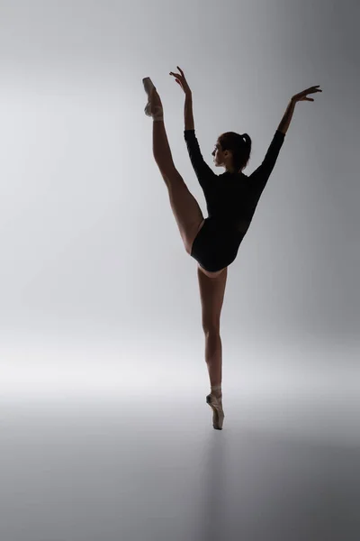 Повна довжина гнучкої балерини в боді-костюмі танцює на темно-сірому — стокове фото