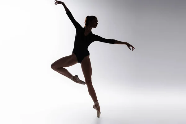 Silueta de joven bailarina en body bailando sobre gris - foto de stock