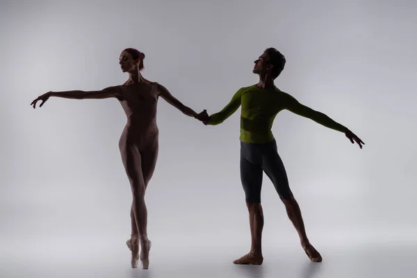 Silhouette einer jungen Tänzerin, die Händchen hält mit Ballerina auf grau — Stockfoto
