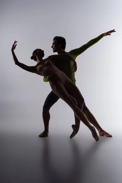 Silhouette einer Balletttänzerin, die eine Ballerina auf dunkelgrau unterstützt — Stockfoto