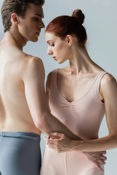 Ballerina senza maglietta che abbraccia una giovane ballerina aggraziata isolata sul grigio — Foto stock