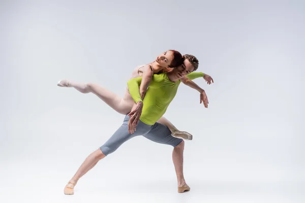 Full length of strong ballet dancer lifting graceful ballerina on grey — Stock Photo
