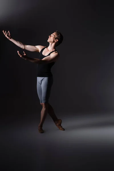 Graceful dancer with outstretched hands performing ballet dance on black — Stock Photo