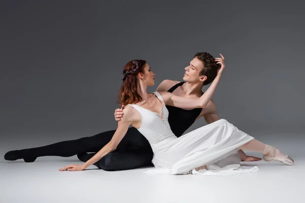 Graceful ballerina in white dress dancing with partner on dark grey — Stock Photo