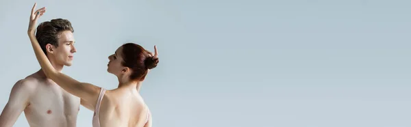 Redhead ballerina looking at shirtless ballet dancer isolated on grey, banner — Stock Photo