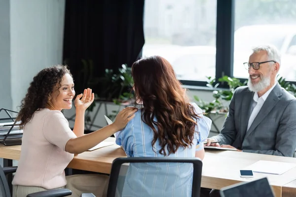 Happy african american woman touching shoulder of girlfriend near real estate agent smiling on blurred background — Stock Photo