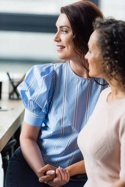 Happy interracial lesbians holding hands while sitting in real estate agency — Stock Photo