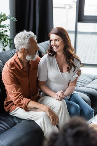 Casal feliz olhando um para o outro enquanto sentado no sofá durante a consulta psicológica — Fotografia de Stock