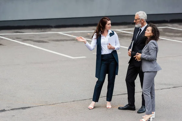 Mujer de negocios afroamericana mirando hacia otro lado cerca de colega de mediana edad y agente inmobiliario señalando con la mano - foto de stock