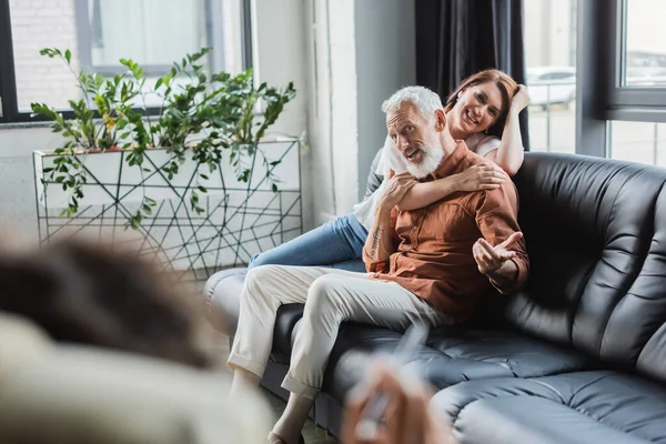 Smiling woman hugging husband talking to blurred african american psychologist during consultation — Stock Photo