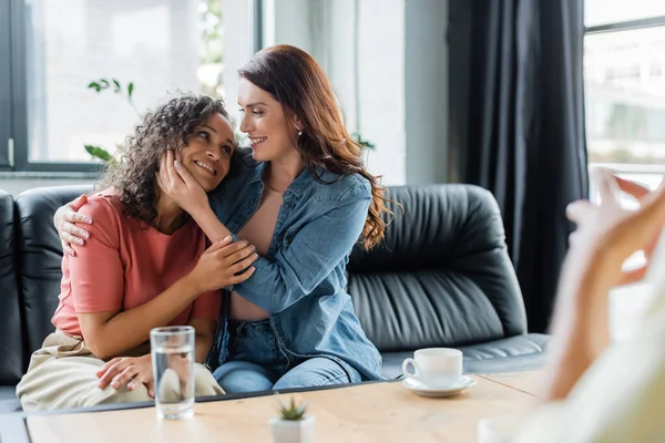 Paar interrassischer lesbischer Frauen umarmen sich auf Couch neben verschwommenem Psychologen im Beratungszimmer — Stockfoto