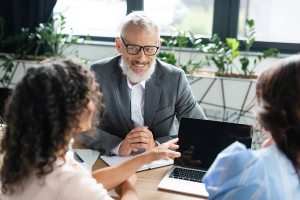 African american woman pointing at laptop with blank screen near lesbian girlfriend and smiling realtor — Stock Photo