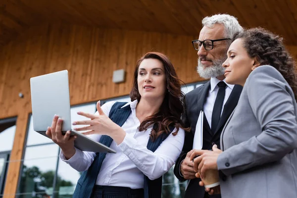 Real estate agent pointing at laptop near interracial business partners outdoors — Stock Photo