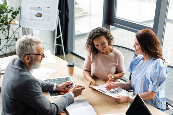 Smiling interracial lesbian women looking at mortgage graphs near real estate broker in office — Stock Photo