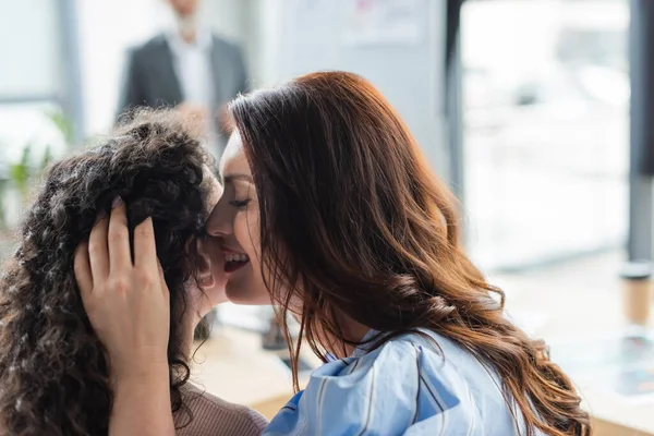 Smiling lesbian woman telling secret to african american girlfriend in real estate agency — Stock Photo