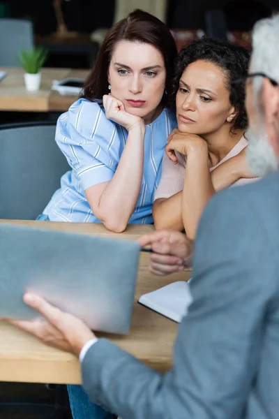 Borrosa agente de bienes raíces apuntando a cuaderno cerca de pareja reflexiva de mujeres lesbianas - foto de stock