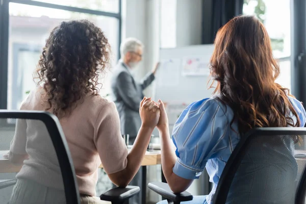 Vista posteriore di interrazziale stesso sesso coppia tenendosi per mano mentre mediatore immobiliare in piedi vicino flip chart — Foto stock