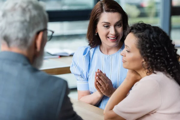 Souriant lesbienne femme montrant s'il vous plaît geste près afro-américaine copine et flou agent immobilier — Photo de stock