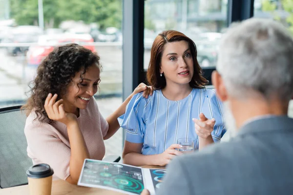 Afroamerikanerin berührt Schulter lesbischer Freundin und zeigt mit Hypothekengrafik auf verschwommenen Makler — Stockfoto