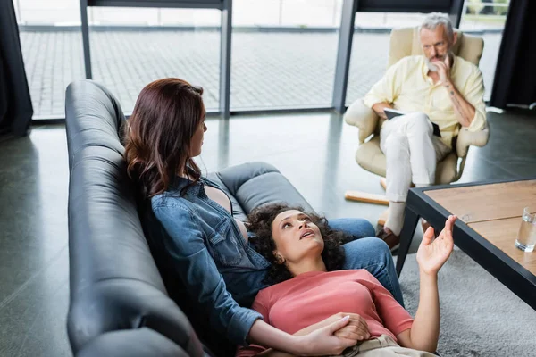 Blurred psychologist listening to african american woman lying on couch near sitting lesbian girlfriend — Stock Photo