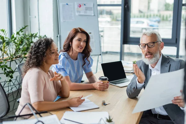 Agente inmobiliario de mediana edad mostrando documento a pareja lesbiana multiétnica en agencia inmobiliaria — Stock Photo