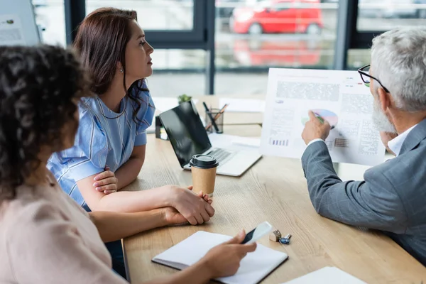 Middle aged sales manager showing mortgage graphs to interracial lesbian couple in real estate agency — Stock Photo
