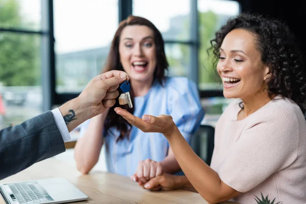 Excited african american woman taking key from real estate broker near happy lesbian girlfriend — Stock Photo