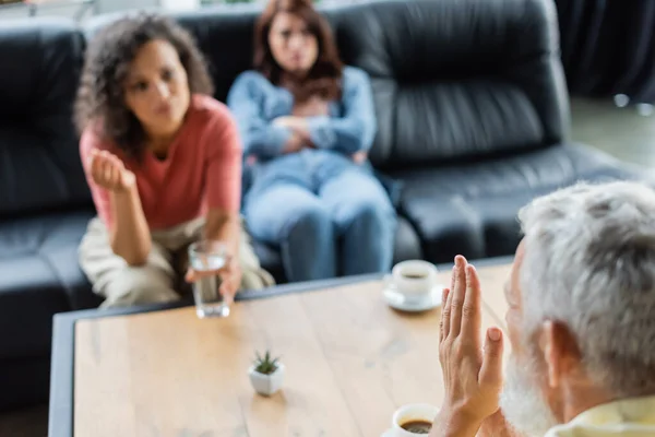 Psicólogo de meia-idade gesticular enquanto conversa com mulheres lésbicas inter-raciais turvas durante a consulta — Fotografia de Stock