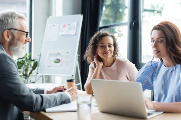 Interracial lesbian couple looking at laptop near blurred realtor — Stock Photo