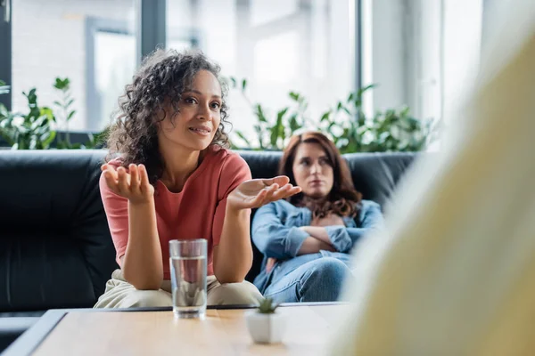 Africana americana mujer apuntando con las manos a borrosa psicólogo cerca ofendido lesbiana novia - foto de stock