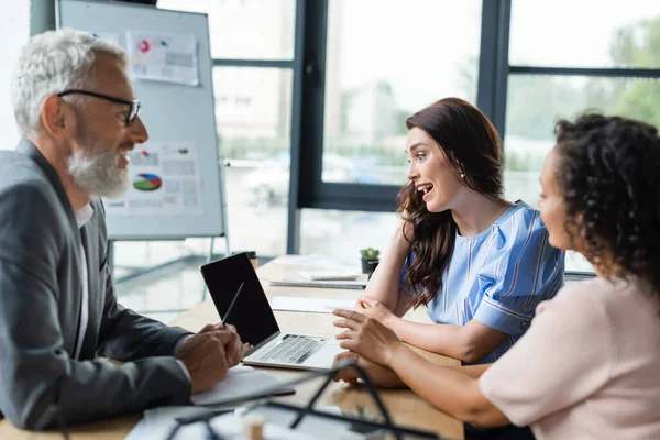 Lesbian african american woman pointing at laptop with blank screen near amazed girlfriend and smiling realtor — Stock Photo