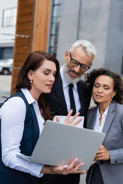 Agente immobiliare mostrando laptop a partner commerciali interrazziali positivi all'aperto — Foto stock