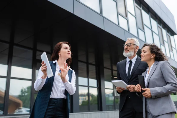 Real estate realtor holding digital tablet and key near pleased interracial business partners — Stock Photo