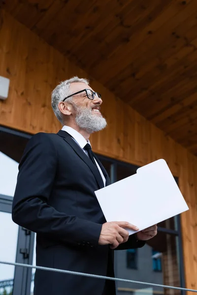 Succès homme d'affaires d'âge moyen avec dossier souriant tout en regardant loin à l'extérieur — Photo de stock