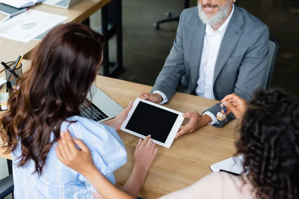 Lächelnder Makler mit digitalem Tablet und leerem Bildschirm in der Nähe multiethnischer lesbisches Paar — Stockfoto