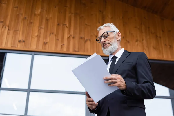 Tiefansicht eines gestandenen Geschäftsmannes in Anzug und Brille, der Dokumente im Freien betrachtet — Stockfoto