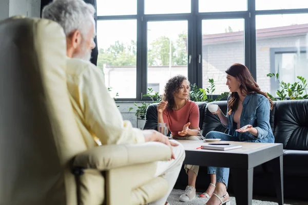 Couple lesbienne multiethnique gestuelle tout en parlant sur le canapé pendant la consultation psychologique — Photo de stock