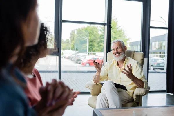 Lächelnder Psychologe im Gespräch mit lesbischem Paar, das Hände auf verschwommenem Vordergrund hält — Stockfoto