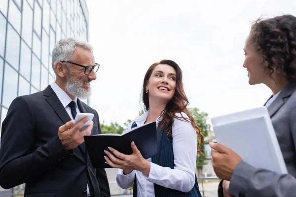 Corredor de bienes raíces feliz con notebook hablando con socios comerciales interracial al aire libre - foto de stock