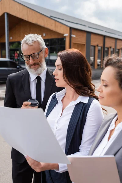 Real estate agent showing plan to interracial business colleagues near blurred building outdoors — Stock Photo